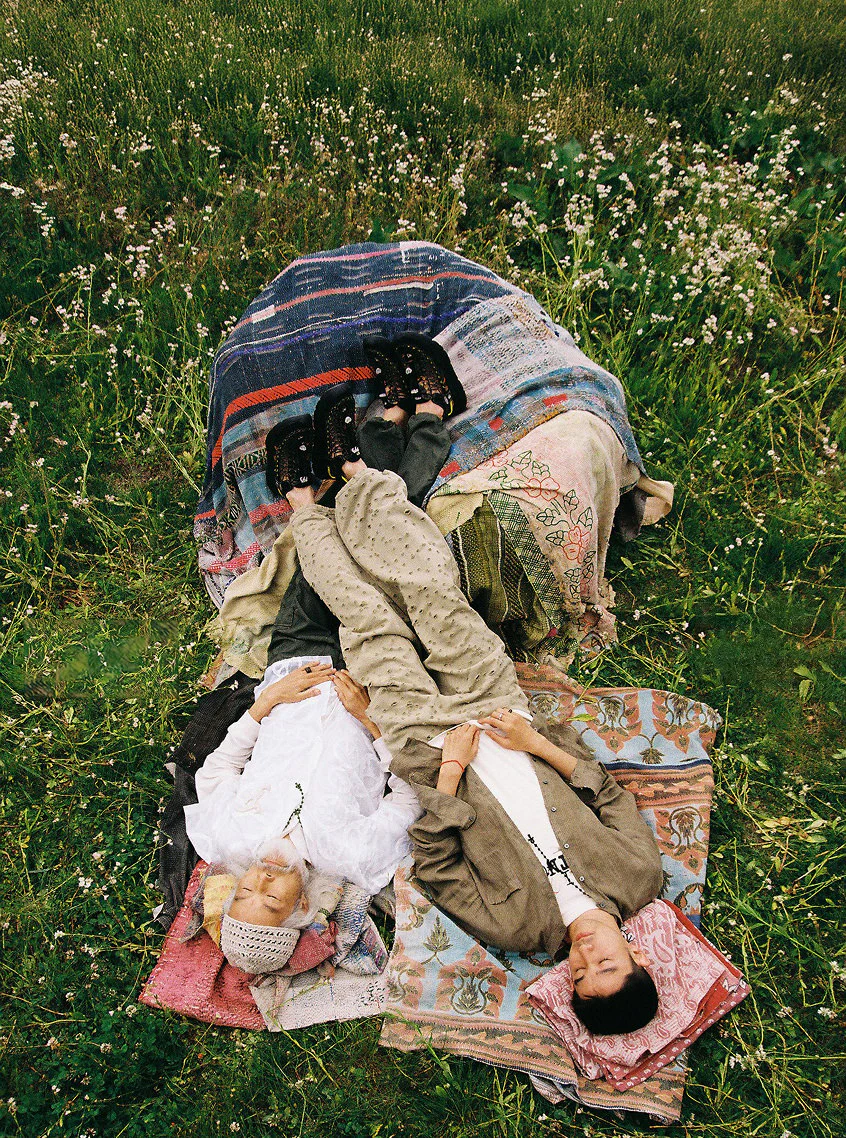Two men laying on picnic blankets in grassy fields with their feet up on a blanket pile while wearing Keen and FAF collaboration Uneek sandals.